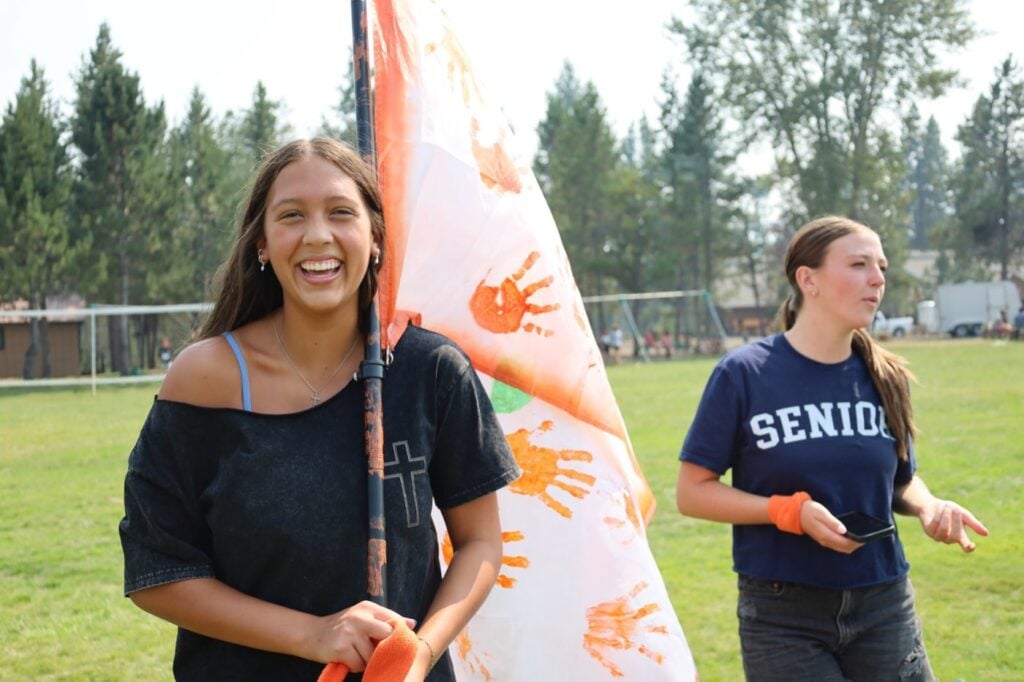 A student laughing as she carries her team flag at camp
